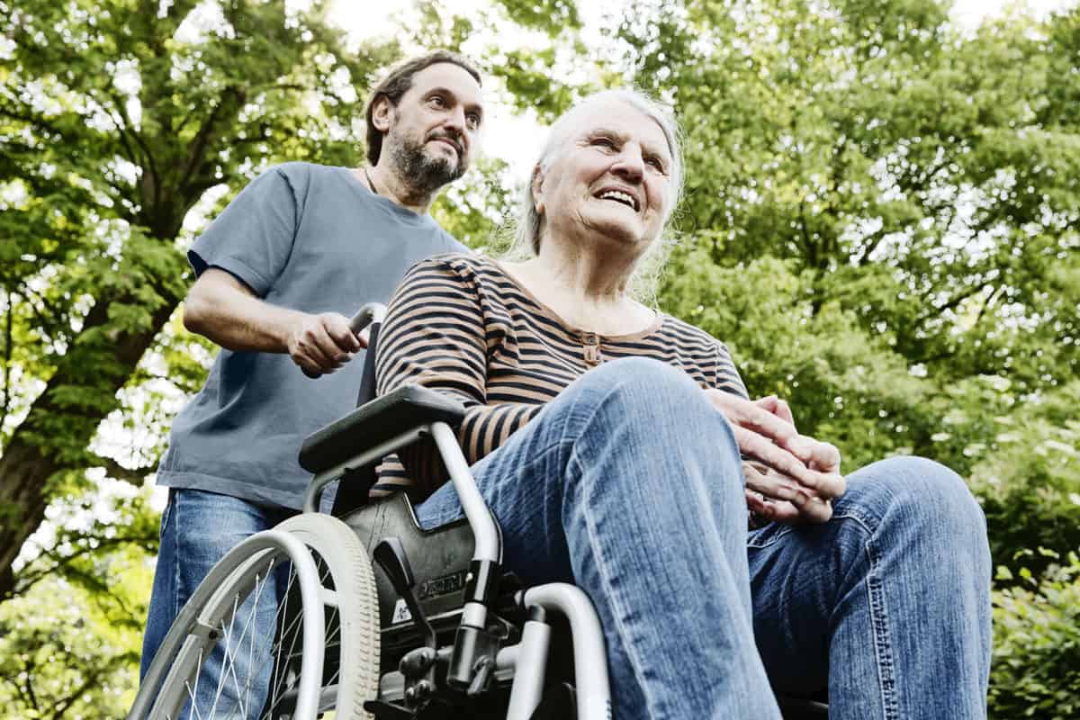 Pflegekraft assistiert älterer Frau im Rollstuhl im Grünen, fürsorgliche Betreuung, ambulante Pflege, Seniorenpflege, liebevolle Pflegeleistungen, Hahne Pflegedienst.