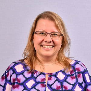 Frau mit Brille und blauer Bluse lächelt freundlich, symbolisiert die persönliche Betreuung im ambulanten Pflegedienst.